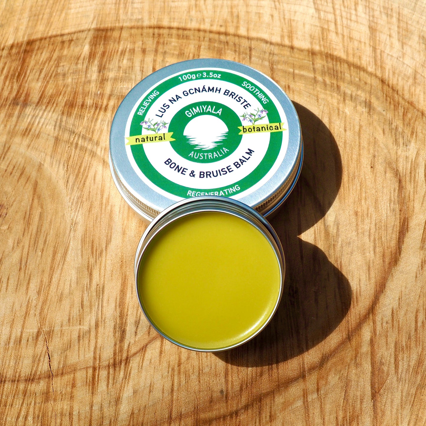 Open tin of bone and bruise balm with visible green cream on a wooden surface