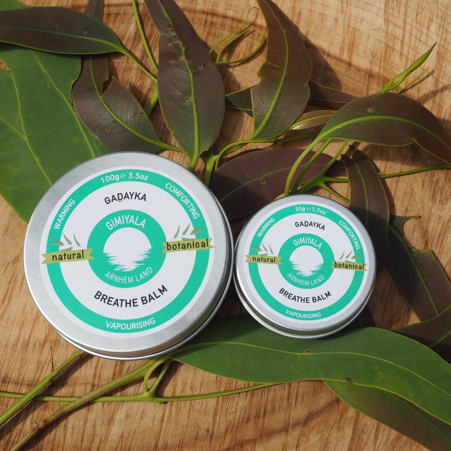Two tins of Gadayka Breathe Balm on a wooden surface with eucalyptus leaves.
