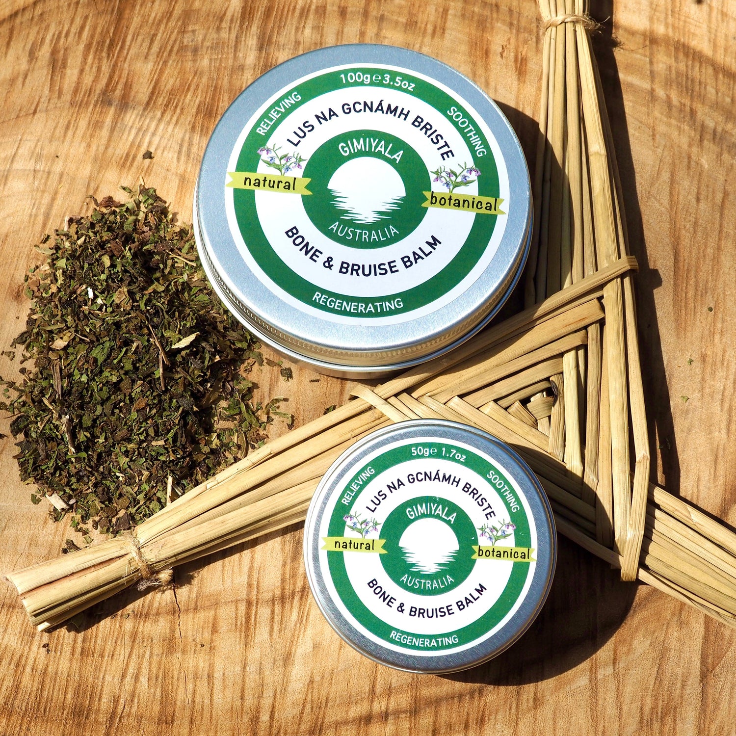 Two tins of Gimiyala Balm on a wooden surface with herbs.