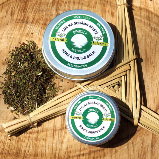 Two tins of Gimiyala Balm on a wooden surface with herbs.